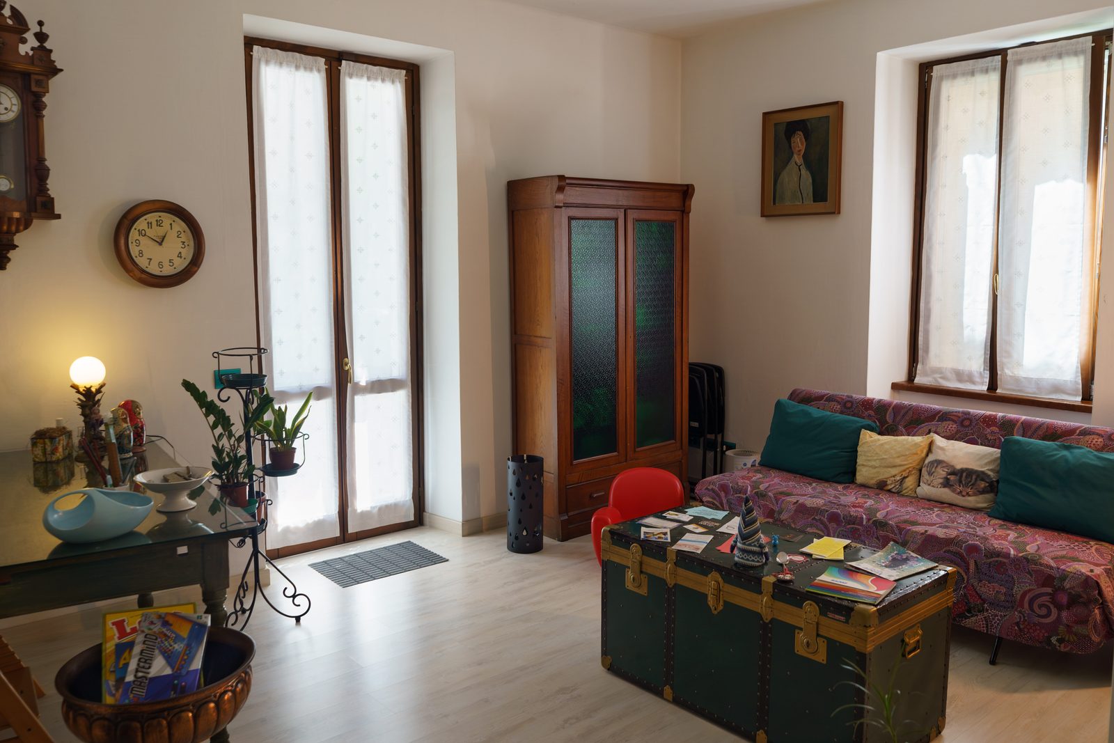 La sala d’attesa: il divano, il baule, l’orologio a pendolo e la luce che entra dalle finestre